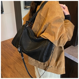 Detail of black leather crossbody bag with metallic lock closure and adjustable strap