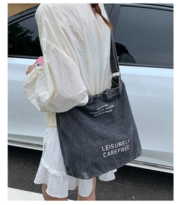 Détail du sac fourre-tout en denim gris foncé avec typographie blanche et large bandoulière