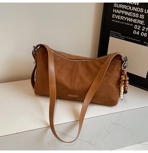 Détail d'un sac à bandoulière en daim marron avec fermeture éclair et breloque perlée
