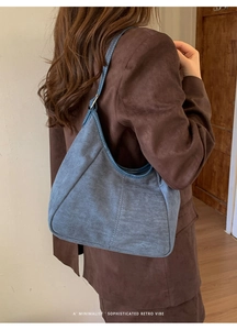Sac croissant en daim bleu porté à l'épaule par un mannequin avec une touche rétro épurée