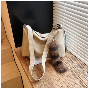 Detail of cream hobo bag with wide shoulder strap and striped faux fur tail pendant