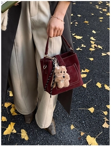 Detail of burgundy matte bucket bag with a teddy bear charm on autumn leaf background