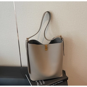 Gros plan d'un sac seau en cuir gris avec fermoir rotatif doré sur un livre