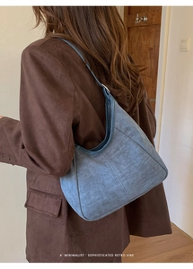Gros plan du sac hobo en daim bleu avec surpiqûres porté à l'épaule du modèle