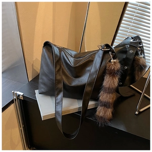 Close-up of large black hobo bag with faux fur charm on a prop book background