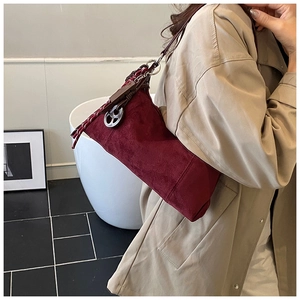 Détail du sac polochon en daim bordeaux avec bandoulière tissée et breloques métal