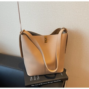 Détail du sac seau en cuir beige avec fermoir doré posé sur un livre au style épuré