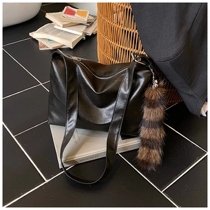 Detailed view of black soft leather tote bag featuring a striped faux fur tail charm accessory