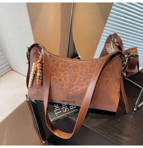 Détail d'un sac bandoulière léopard avec pendentif en bois et plaque logo en métal