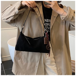 Détail du sac bandoulière en daim noir avec pendentif porté sur un trench-coat kaki