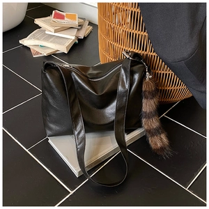 Detail of black faux leather tote with silver zipper and a striped plush tail pendant