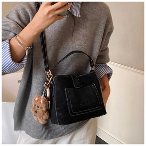 Detail of black suede handbag with white stitching and cute brown teddy bear charm