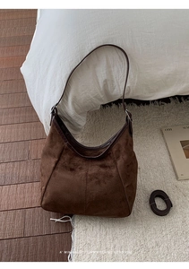 Sac hobo en daim marron foncé avec bandoulière en cuir sur un tapis blanc moelleux