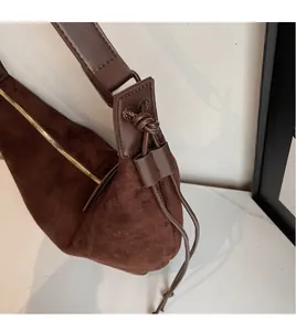 Detail of dark brown suede underarm bag featuring a wide strap and gold metal zipper