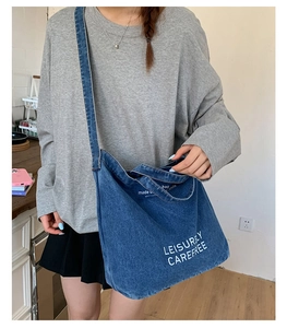 Détail du sac cabas en jean bleu avec texte Leisurely Carefree porté en bandoulière