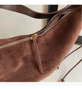 Close-up of smooth gold metal zipper and suede texture on dark brown underarm bag