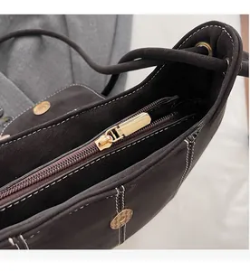 Détail d'un sac seau en daim marron foncé avec fermeture éclair dorée et coutures blanches