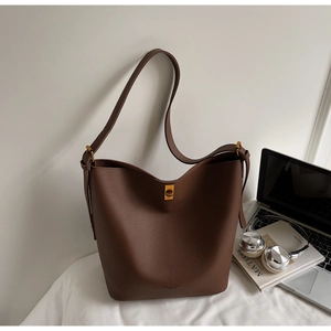 Détail du sac seau en cuir marron foncé avec fermoir doré et objets du quotidien