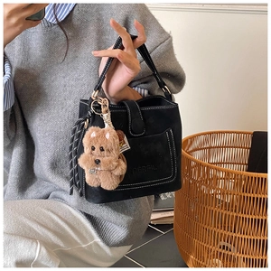 Detail of black matte bucket bag featuring white contrast stitching and plush dog charm
