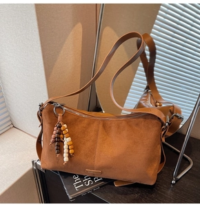 Détail d'un sac bandoulière en daim marron avec breloque bohème et plaque logo en métal