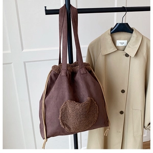 Detail of a large brown suede bucket bag with plush heart applique on a garment rack