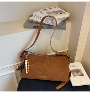 Détail d'un sac à épaule en daim marron avec couture verticale et breloque à pompon