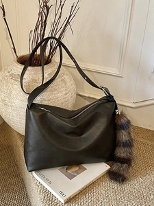 Retro black leather tote bag with fluffy striped tail charm against a white relief wall