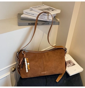 Détail du sac à bandoulière en daim marron avec gland perlé et logo sur fond de livres