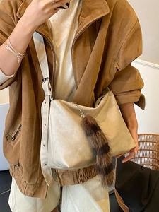 Minimalist beige crossbody bag with wide strap and fuzzy charm pendant on display