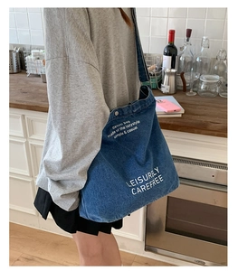 Détail du grand sac cabas en denim bleu foncé avec imprimé texte blanc et bouton-pression