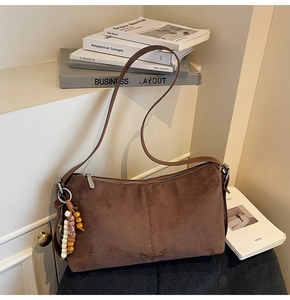 Détail d'un sac bandoulière en daim marron avec pendentif en perles et logo métallique