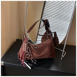 Détail d'un sac hobo en daim marron avec pendentif chocolat et boucles en métal argenté