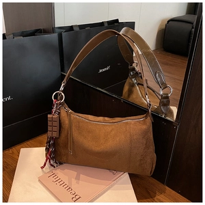 Gros plan d'un sac bandoulière en daim marron avec pendentif chocolat et pompon tissé