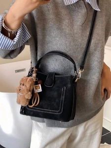 Retro black suede bucket bag with contrast stitching and plush bear charm shown on model