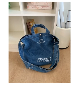 Détail du grand sac cabas en jean bleu avec lettrage artistique blanc et fermoir magnétique