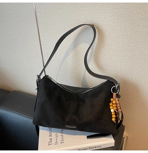 Détail du sac hobo en daim noir avec fermeture éclair argentée et gland à perles