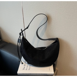 Detail of black suede hobo bag with tassel drawstring, resting on a white book