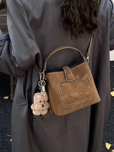 Vintage brown suede handbag with dog charm and strap on grey coat background