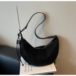 Close-up of black suede crescent bag featuring decorative knot and textured material