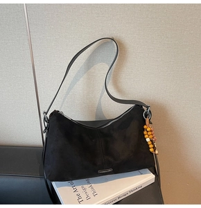 Détail du sac à bandoulière en daim noir avec breloque en bois posé sur des livres de design
