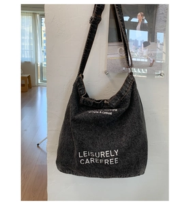 Détail du sac à bandoulière en denim noir délavé avec texte blanc décontracté