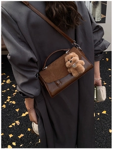Detail einer dunkelbraunen Leder-Umhängetasche mit Bärenanhänger auf Herbststraße