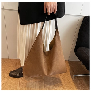Detail of a large brown suede tote bag with black wide leather handles for daily commuting