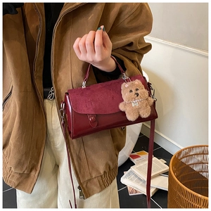 Nahaufnahme der weinroten quadratischen Tasche mit Lederstruktur und Bären-Anhänger