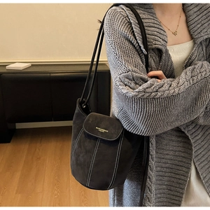 Détail du sac seau en daim gris foncé avec surpiqûres blanches et logo doré