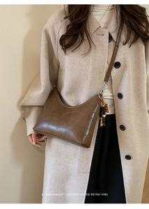 Detail view of a brown retro crossbody bag with a unique wooden bead charm on a beige coat