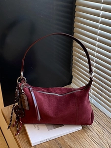 Sac hobo vintage en daim bordeaux avec fermeture éclair argentée sur table en bois