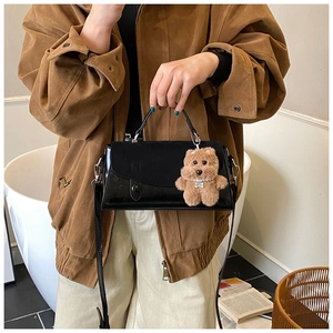 Detail der schwarzen glänzenden Handtasche mit braunem Plüschbären-Anhänger und Riemen
