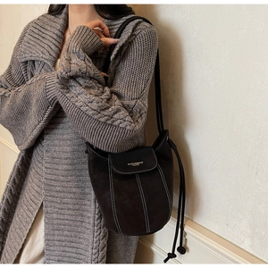 Détail du sac seau en daim mat avec surpiqûres blanches et logo imprimé sur le rabat