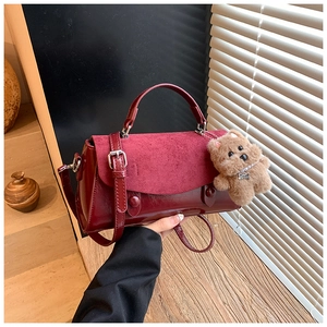 Detail der weinroten Tasche aus mattem und glänzendem Leder mit Plüschbär-Anhänger